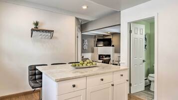 A modern kitchen with a marble countertop, a bowl of fruit, and a black leather chair.