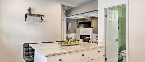A modern kitchen with a marble countertop, a bowl of fruit, and a black leather chair.