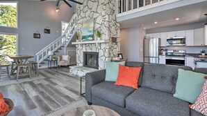 A spacious living area with a stone fireplace, grey sofa, and a staircase leading to a balcony. - Boat Dock, Furnished Deck! Lakefront Ozarks Home (Lake Ozark)