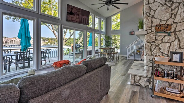 A spacious living area with a large gray sofa, a stone accent wall, and a view of the outdoors. - Boat Dock, Furnished Deck! Lakefront Ozarks Home (Lake Ozark)