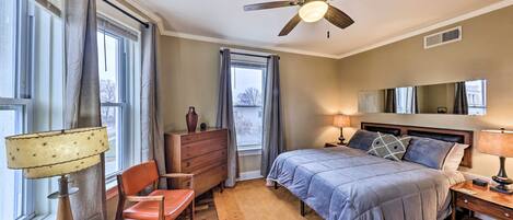 A bedroom with a bed, a desk, a chair, a dresser, and a ceiling fan.