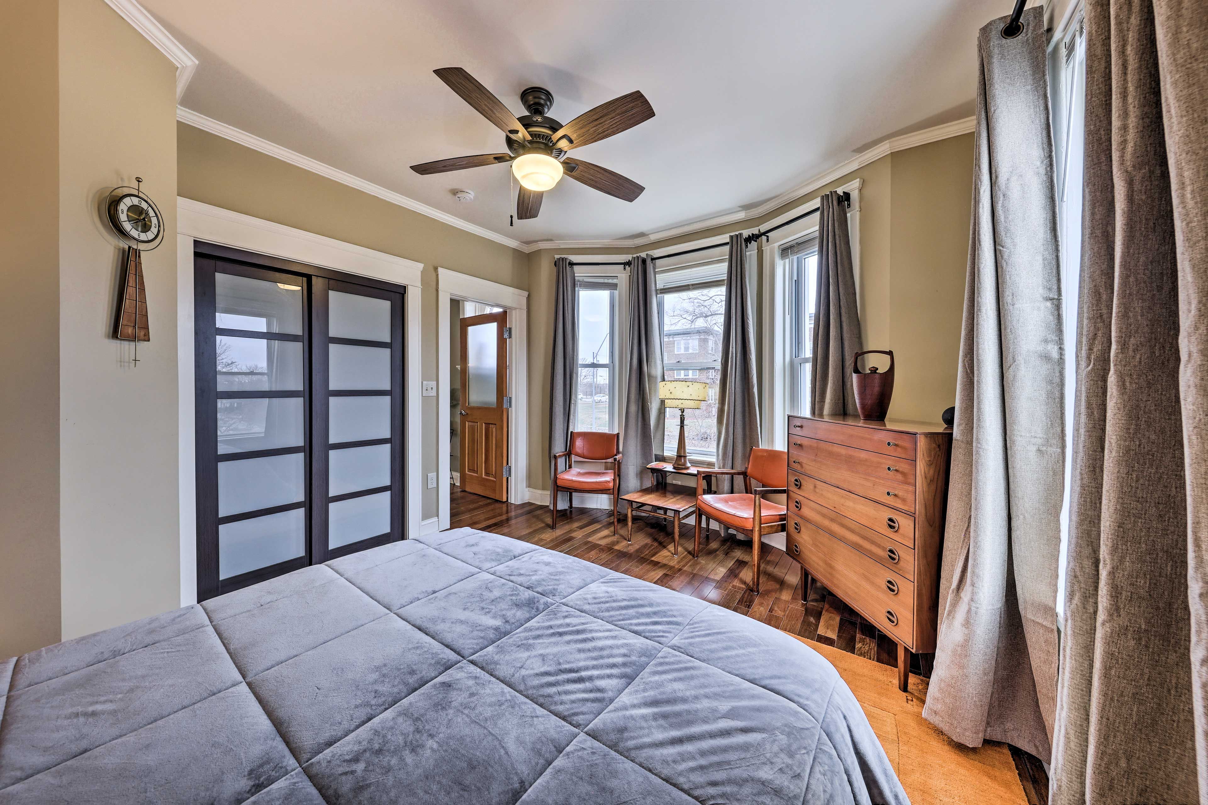 A bedroom with a large bed, a ceiling fan, a dresser, and a window with curtains.