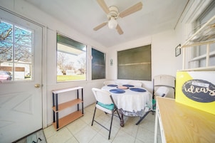 Una habitación con ventilador de techo, una mesa con mantel blanco y individuales azules, una silla y una estantería.