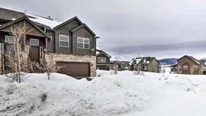 Zona residencial com casas, chão coberto de neve e montanhas ao fundo.
