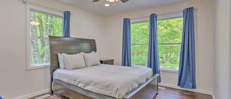 A bedroom with a bed, nightstands, a ceiling fan, and large windows with curtains.