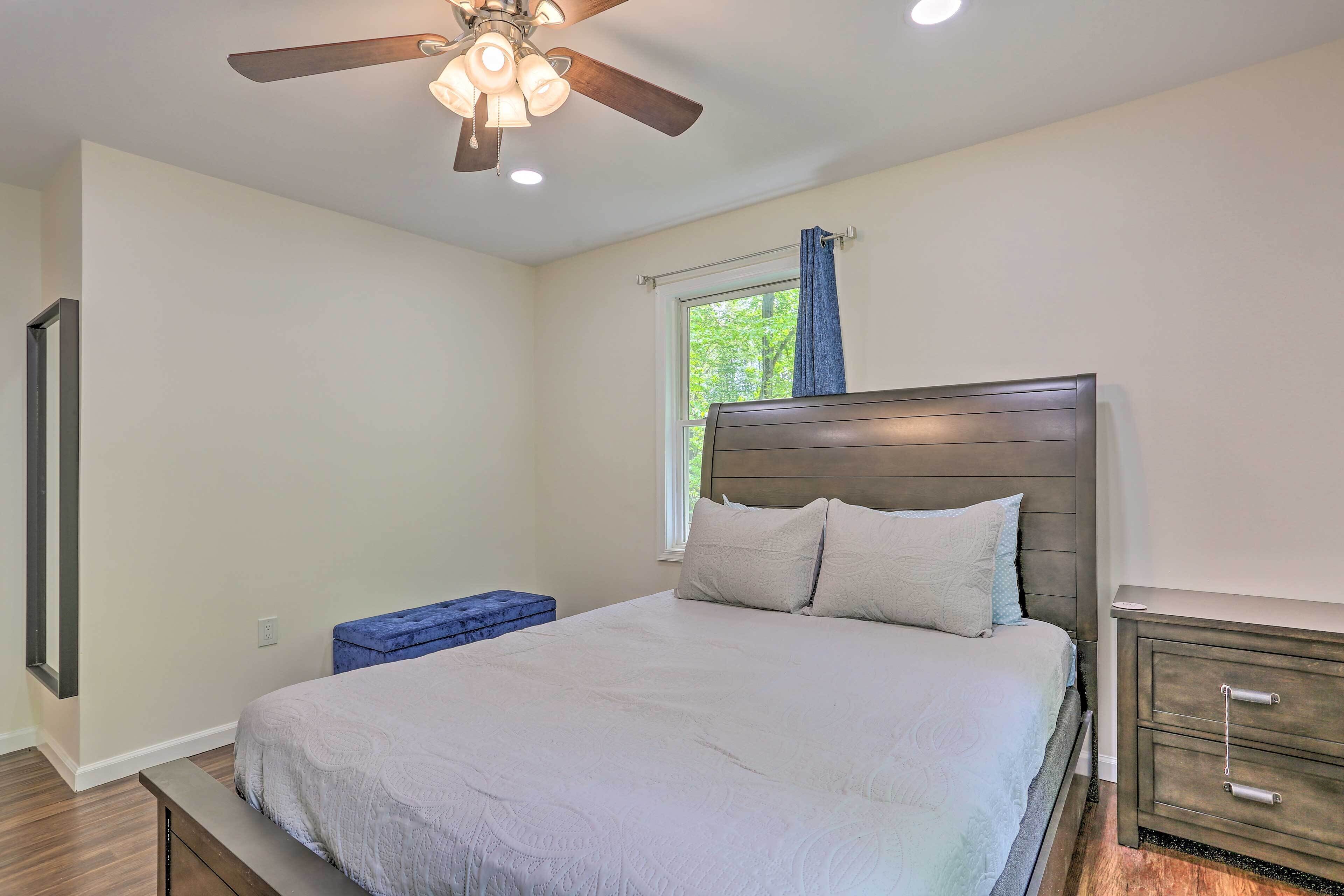 A bedroom with a bed, a nightstand, a dresser, a ceiling fan, and a window with a view of trees.