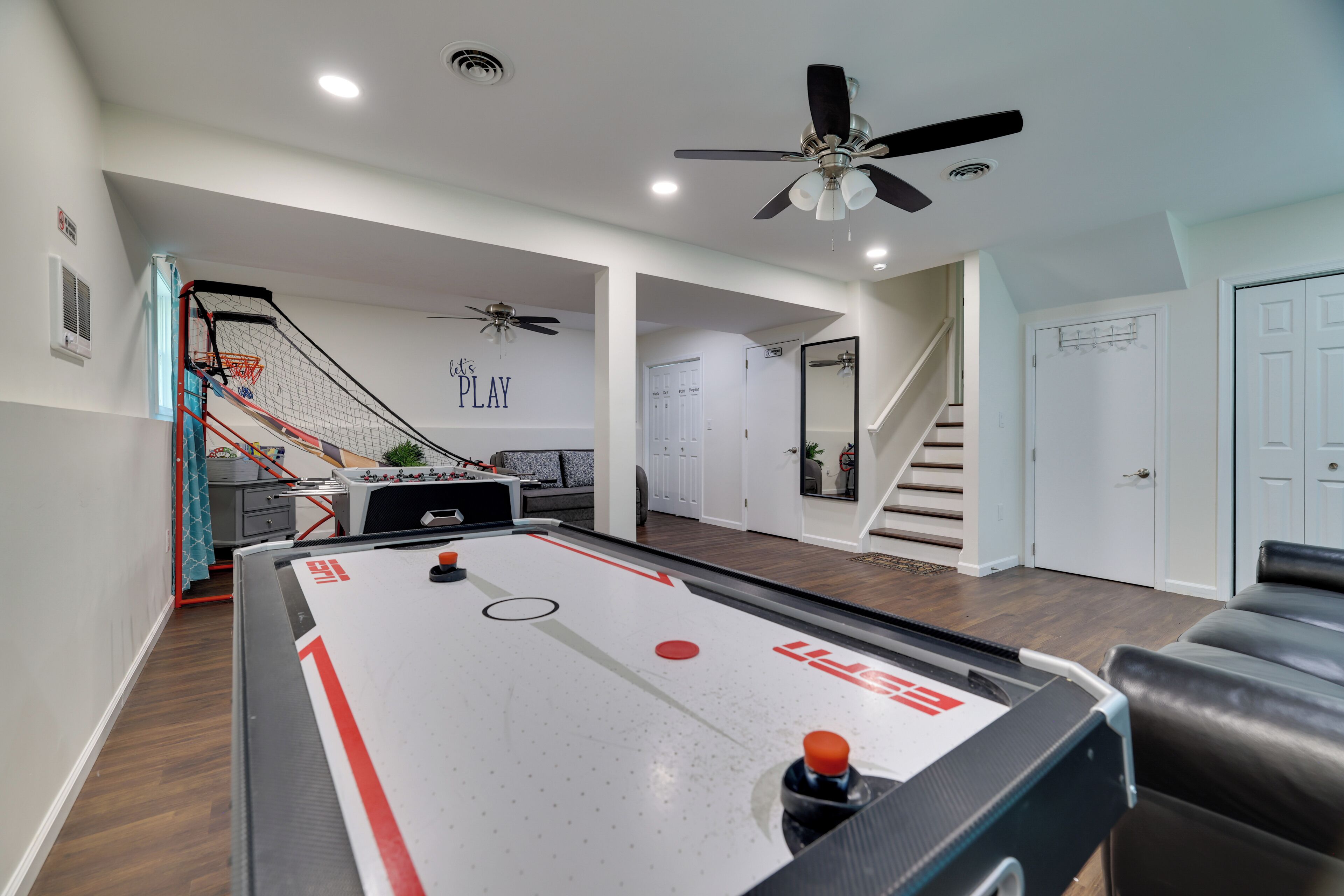 Ett rymligt inomhusområde med ett shuffleboard-bord, en takfläkt och en trappa som leder till en annan våning.