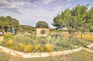 Zona ajardinada con un letrero central, rodeada de diversas plantas y árboles.