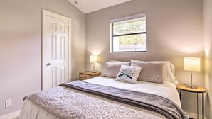 Quarto com uma cama, duas mesas de cabeceira com luminárias, uma janela e uma porta.