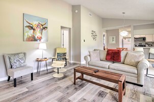 Una sala de estar moderna con una mesa de centro de madera, un sofá y una silla. Hay un cuadro de una vaca en la pared, una lámpara y una pequeña mesa con una silla.