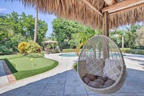 Una poltrona sospesa con cuscini, una piccola piscina e un giardino curato con un putting green.