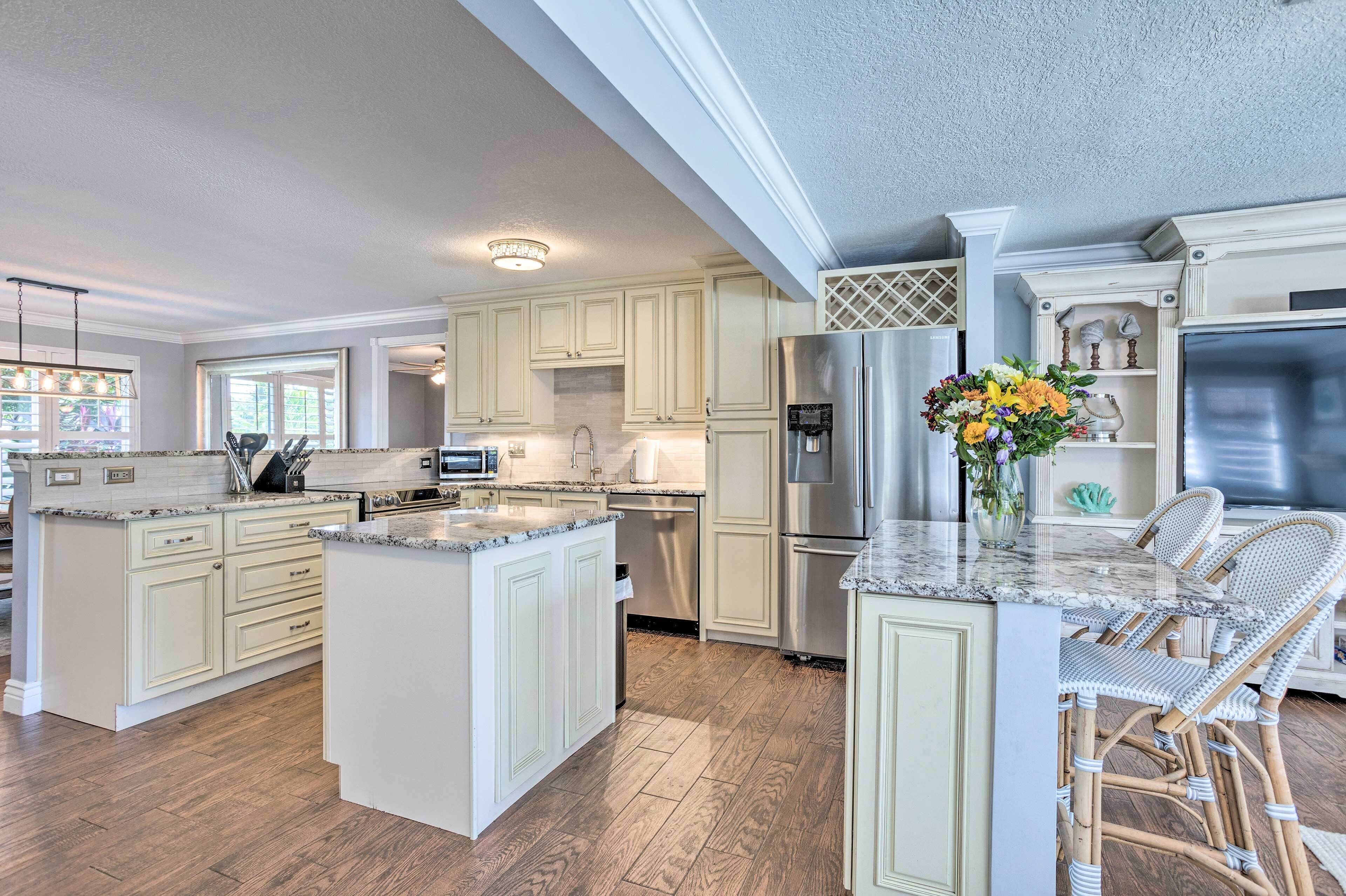 A spacious kitchen with white cabinetry, a large island, and a stainless steel refrigerator.