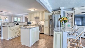 A spacious kitchen with white cabinetry, a large island, and a stainless steel refrigerator. - Poolside Paradise w/ Tropical Hut in Palm Beach (Palm Beach Gardens)