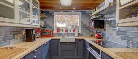 A kitchen with grey cabinets, wooden countertops, a built-in oven, and a window with a view of the outside.