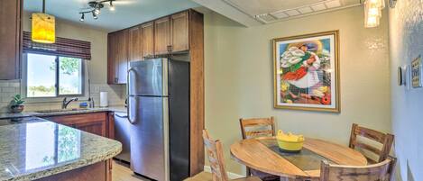 A kitchen with granite countertops, a stainless steel refrigerator, wooden cabinets, and a dining area with a wooden table and chairs.