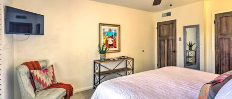 A bedroom with a bed, a chair, a TV mounted on the wall, a ceiling fan, and a framed picture on the wall.
