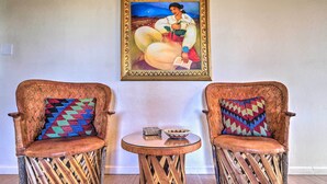 Two woven chairs with colorful cushions, a small round table with a bowl and a box, and a framed painting on the wall. - Traditional-style Adobe Casita - Walk to Dtwn (Santa Fe)
