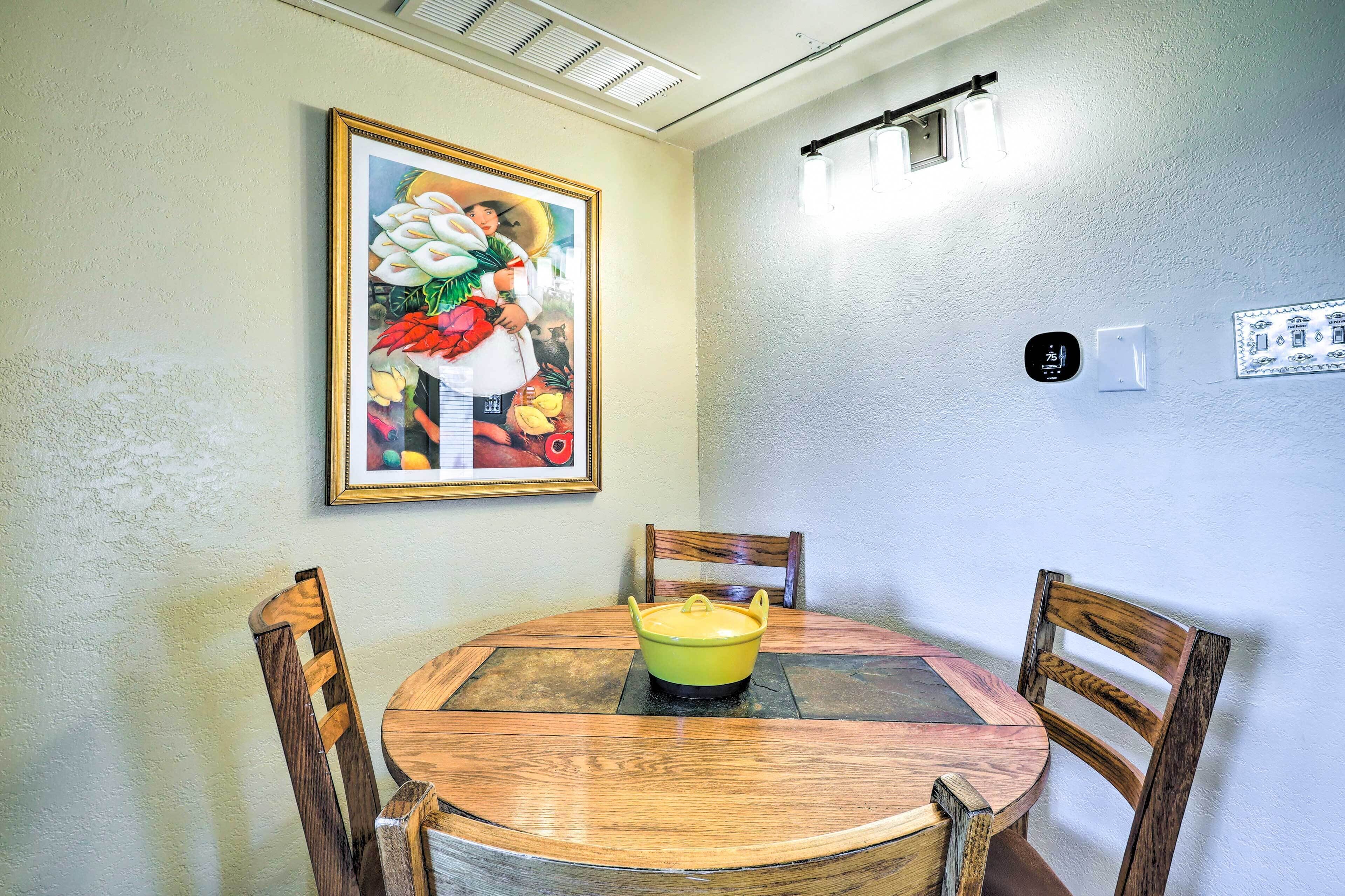 Un comedor con una mesa redonda de madera, dos sillas de madera, una olla amarilla y un cuadro en la pared.
