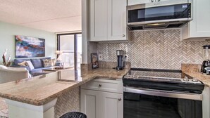 Una cucina moderna con mobili bianchi, zoccolo a mosaico a spina di pesce, forno a microonde integrato e piano cottura in acciaio inossidabile.