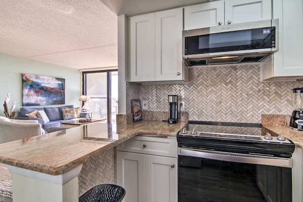 A modern kitchen with white cabinets, a herringbone-patterned backsplash, a built-in microwave, and a stainless steel stove. - Beach & Pool Views! Family Condo in Golden Sands (Ocean City)