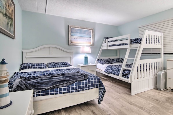 A bedroom with a single bed, a bunk bed, a nightstand with a lamp, and a wall-mounted picture. - Beach & Pool Views! Family Condo in Golden Sands (Ocean City)