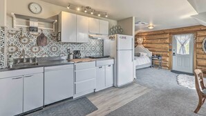 A modern kitchen with white cabinets, a stainless steel sink, and a refrigerator. There is a clock on the wall and a decorative backsplash. - Fraser Couple's Hideaway w/ Indian Peaks View (Fraser)