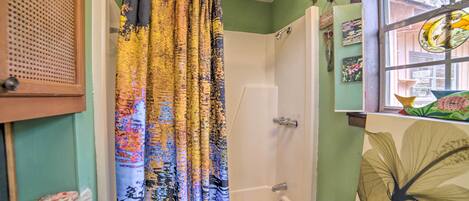 A bathroom with a shower, toilet, and a window with artwork.
