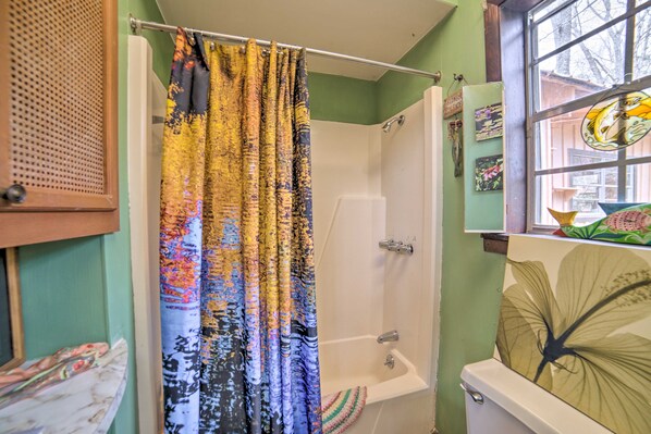 Une salle de bain avec douche, toilettes et une fenêtre décorée d’une œuvre d’art.