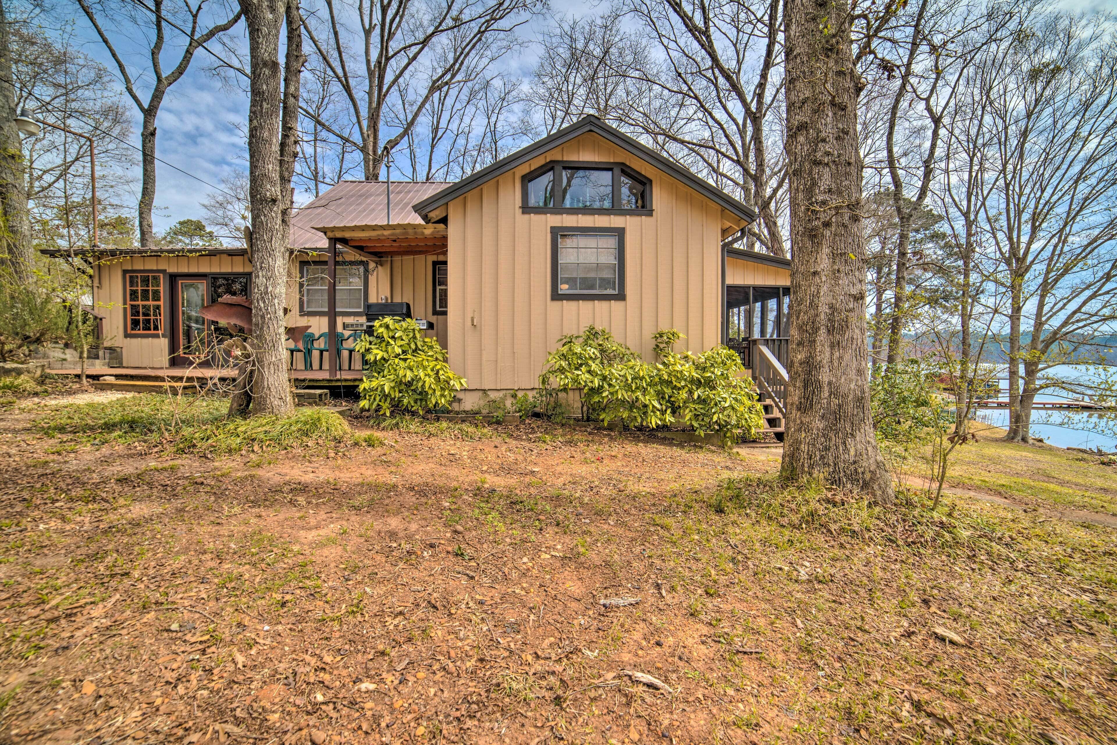 A two-story cabin with a large deck, surrounded by trees and a view of a body of water.
