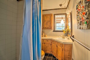 Une salle de bain avec un rideau de douche, des meubles en bois, un lavabo et une fenêtre avec des stores.