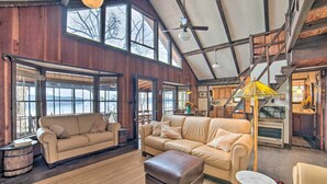 A spacious living room with large windows, a high ceiling, and a cozy fireplace. - Authentic Retreat w/ Private Dock on Coosa River! (Shelby)