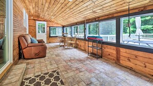 Een houten cabin interieur met een stenen vloer, een leren bank, een eettafel met stoelen en grote ramen met uitzicht op de omgeving.