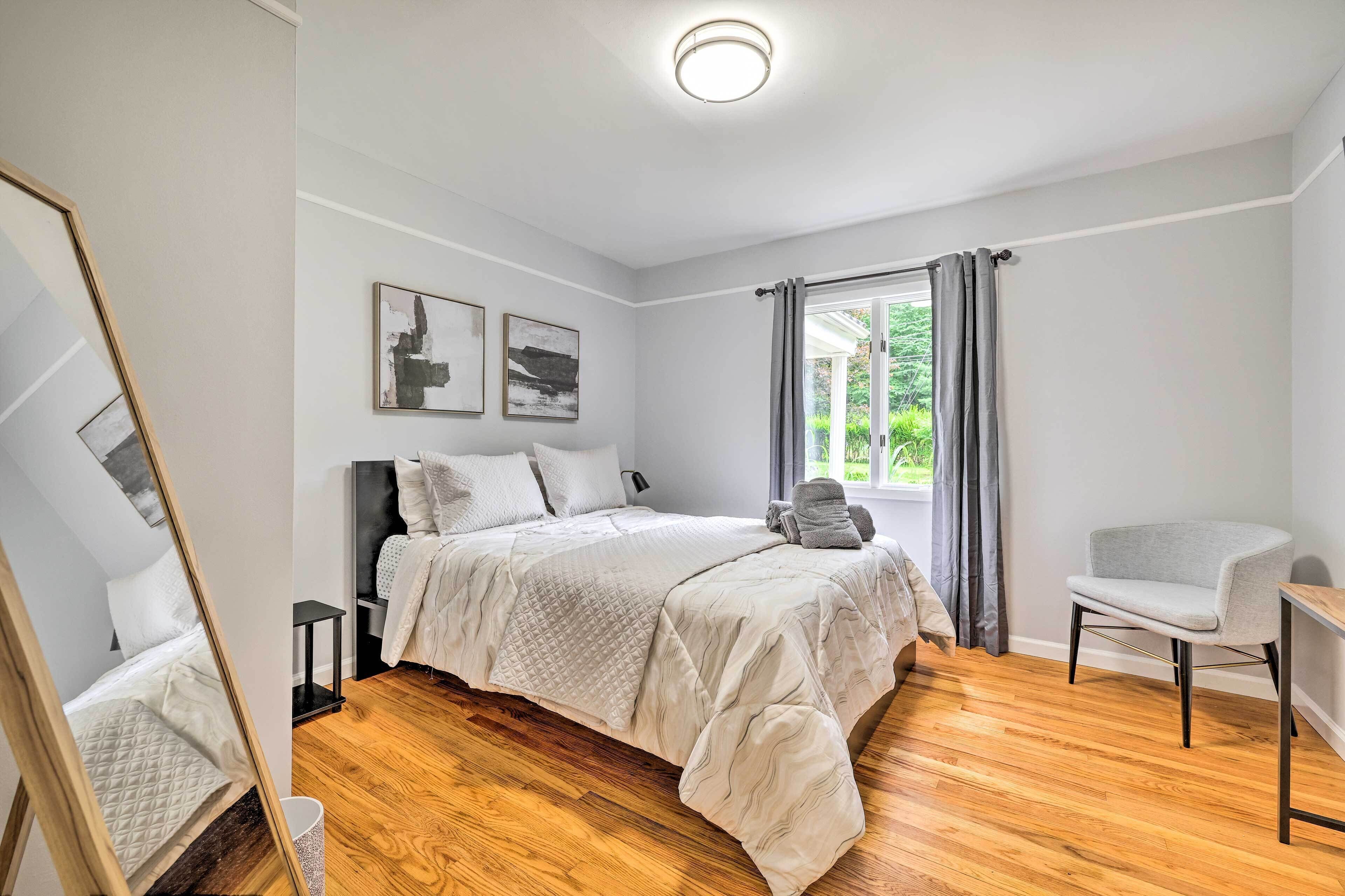 A bedroom with a bed, a chair, a small table, and a window with curtains.