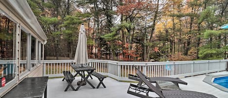 A covered outdoor deck with a pool, lounge chairs, and a table with an umbrella.