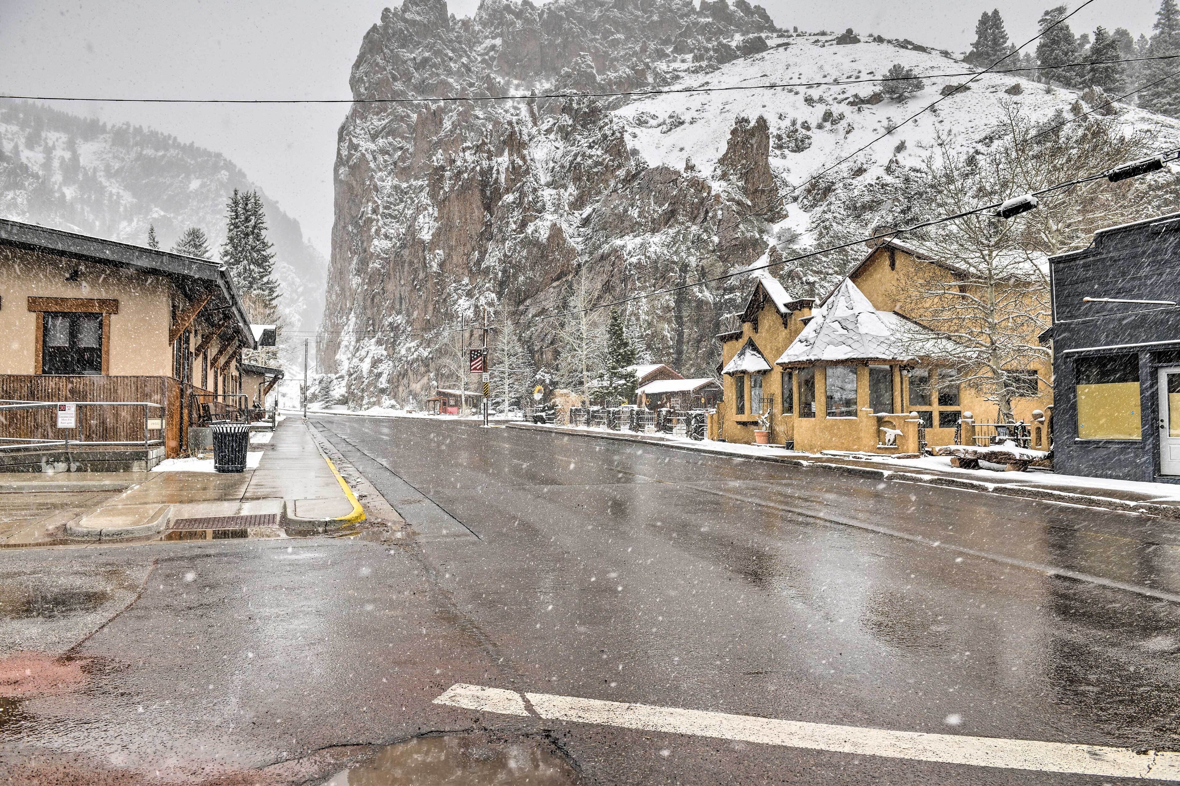 A snow-covered street with buildings, including a wooden structure with a balcony and a yellow building with a snow-covered roof.