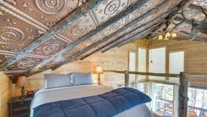 Un dormitorio de cabaña de madera con una cama grande, una mesita de noche, una lámpara y vistas al exterior.