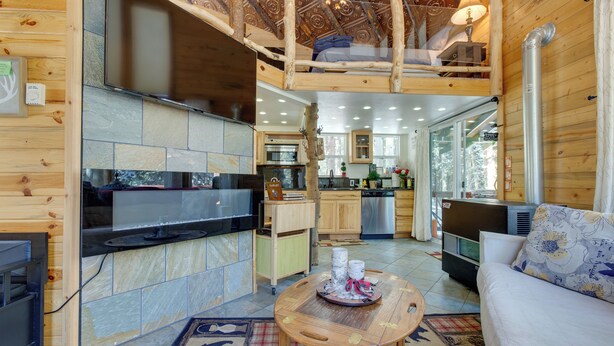 Acogedor interior de cabaña con chimenea de piedra, muebles de madera y zona de cocina.