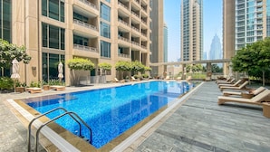 Une piscine avec des chaises longues et, au fond, un bâtiment doté de nombreux balcons.