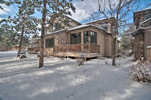 Una casa de dos pisos con balcón y porche cubierto, rodeada de árboles cubiertos de nieve y un cielo despejado.