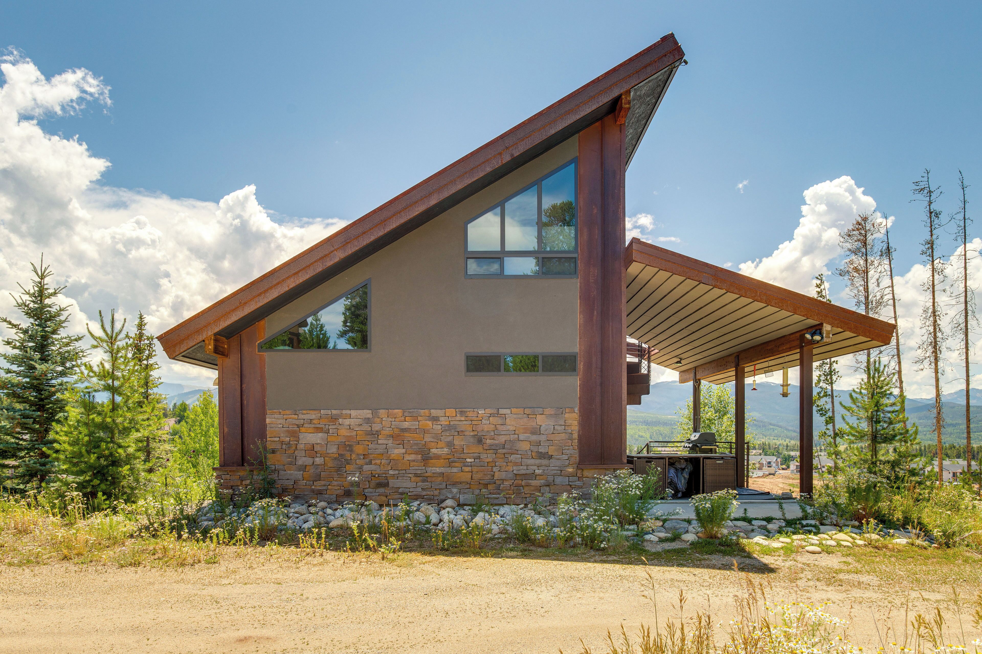 A modern house with a stone facade, large windows, and a covered patio area.