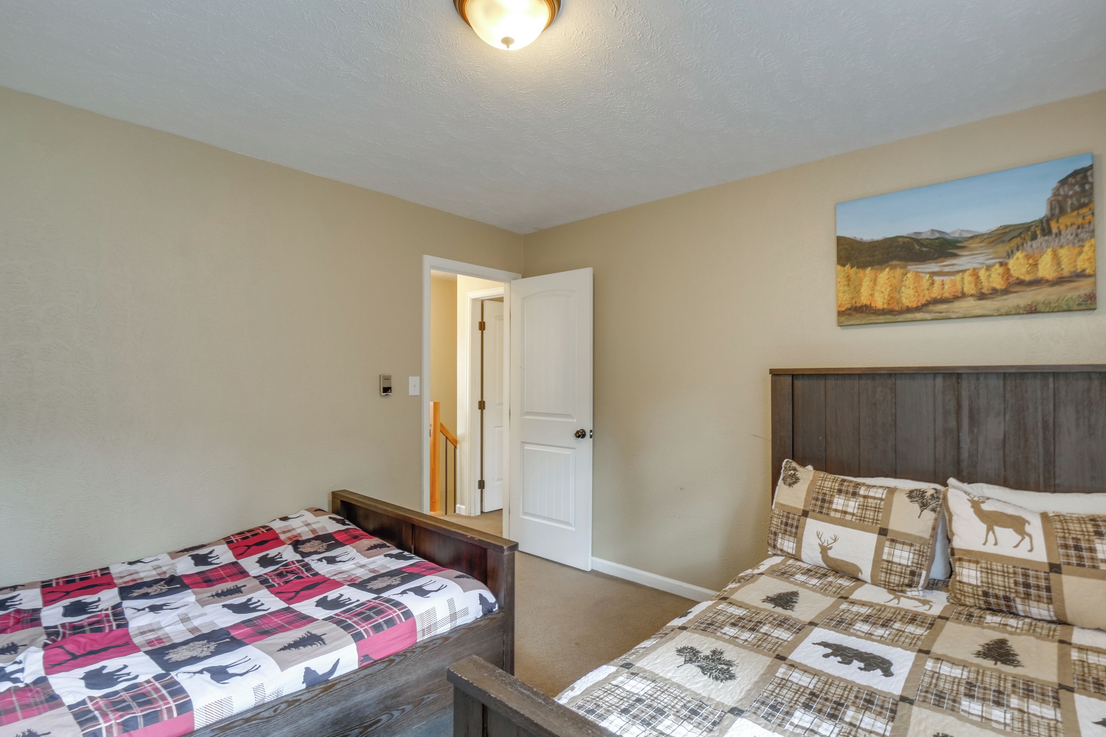 A bedroom with two beds, a painting on the wall, and a door leading to another room.