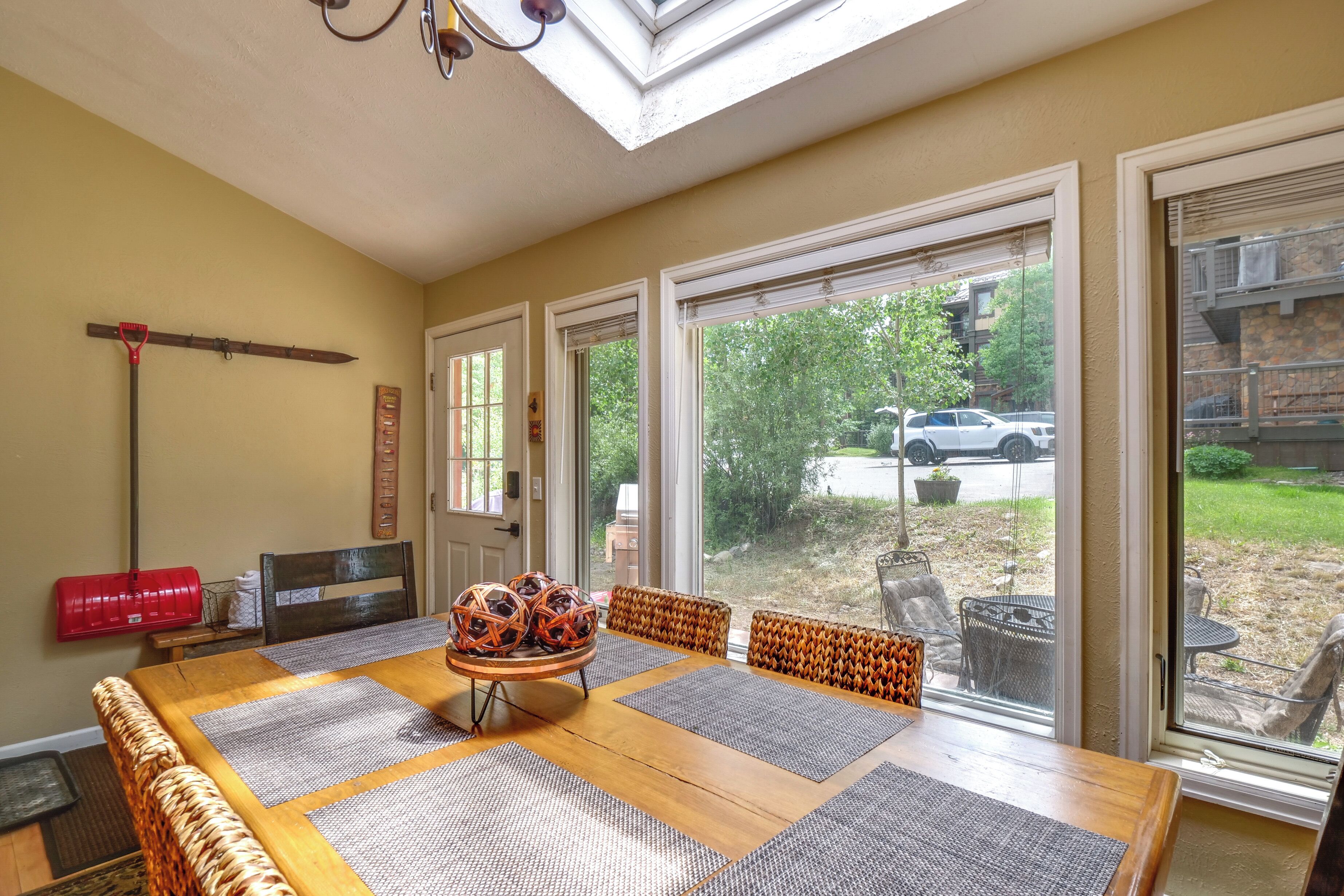 A dining area with a wooden table, woven chairs, and a view of the outdoors through large sliding glass doors.