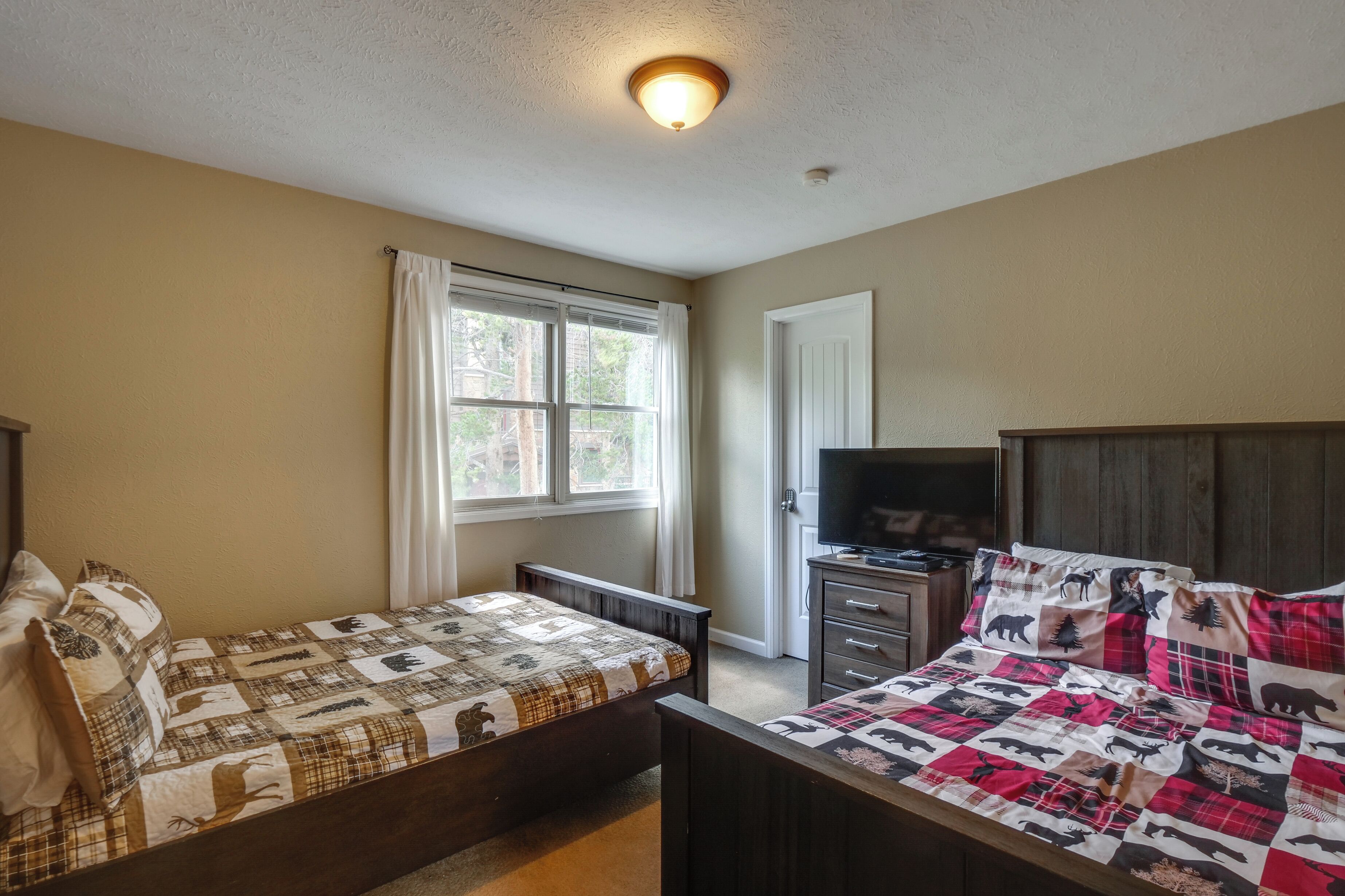 A bedroom with two beds, a TV, and a window with curtains.