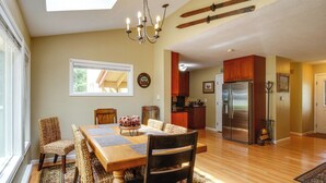 Un comedor con mesa y sillas de madera, una araña y vistas a la cocina y el salón.