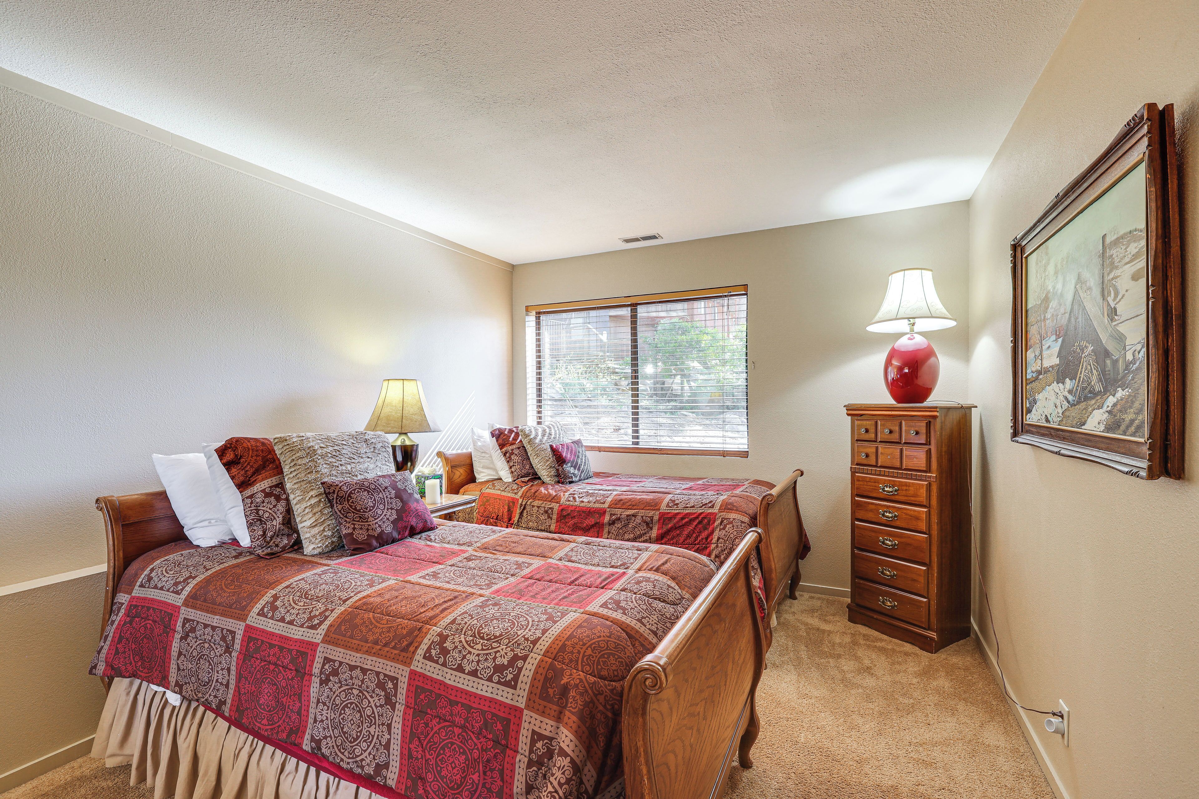 A bedroom with two wooden beds, a dresser, a window with blinds, and a painting on the wall.