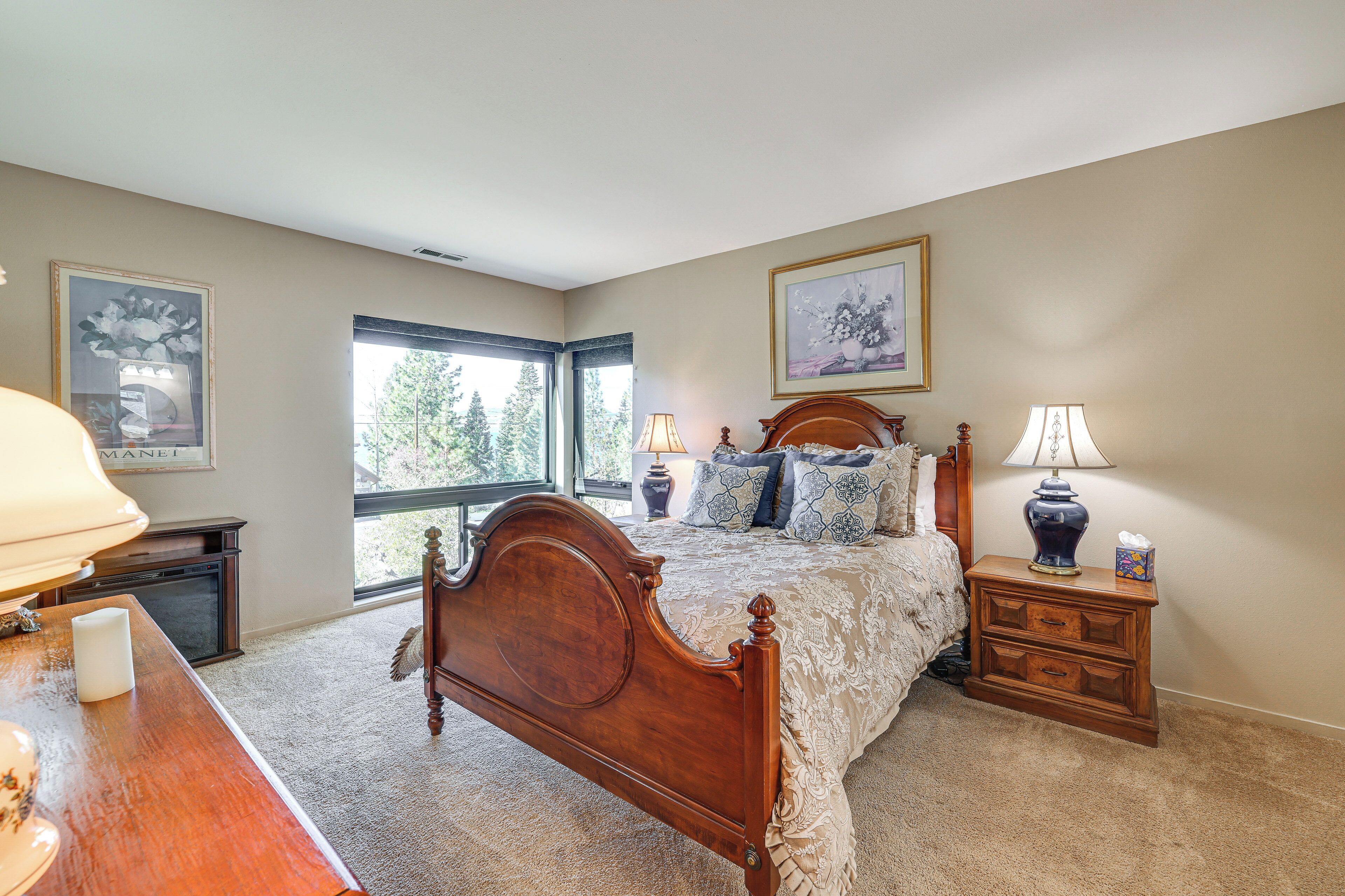 A bedroom with a wooden bed, two bedside tables with lamps, a nightstand, and two framed pictures on the walls.