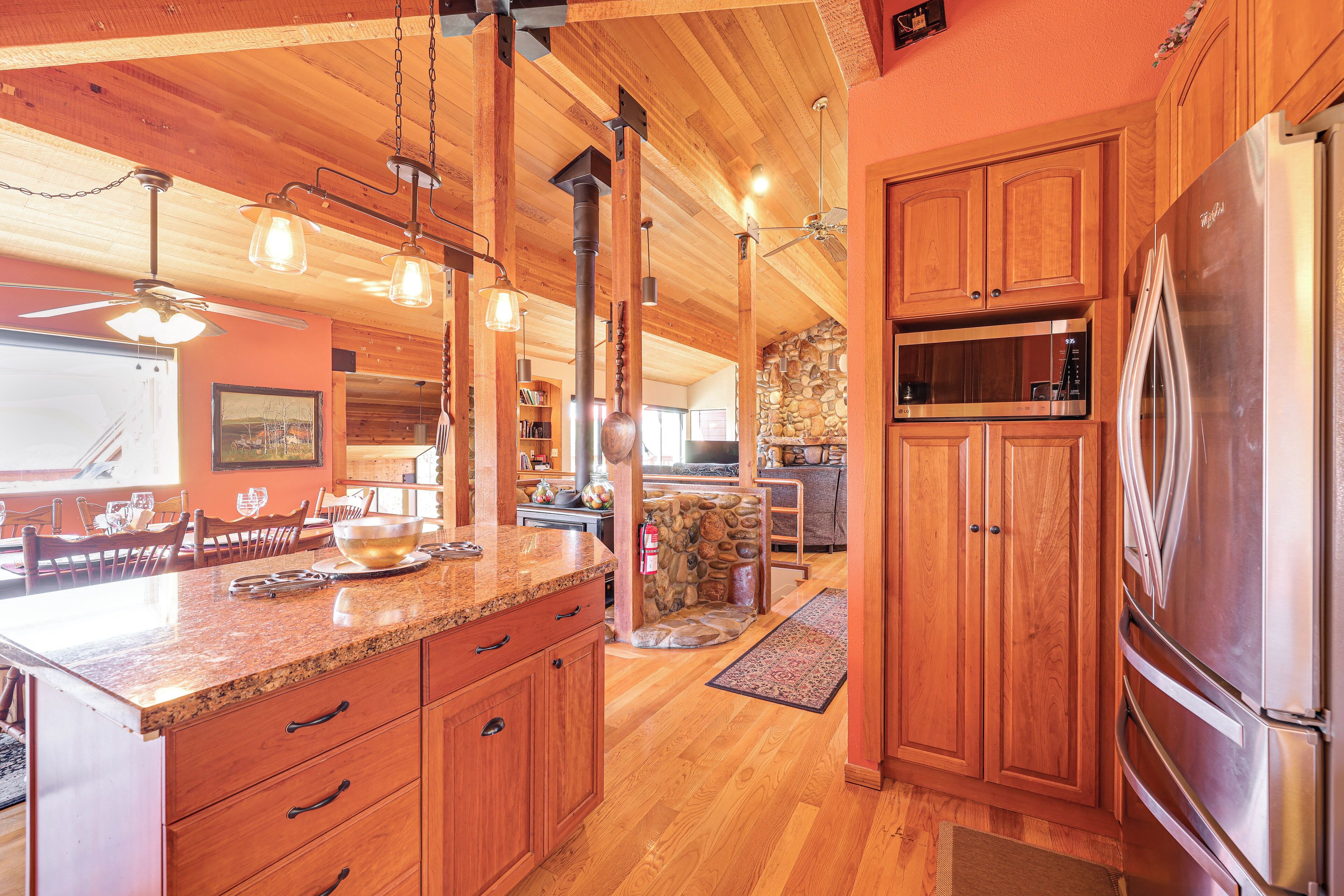 Eine geräumige Küche mit Holzschränken, einer Granitarbeitsplatte und modernen, edlen Edelstahlgeräten, darunter ein Kühlschrank und eine Mikrowelle.