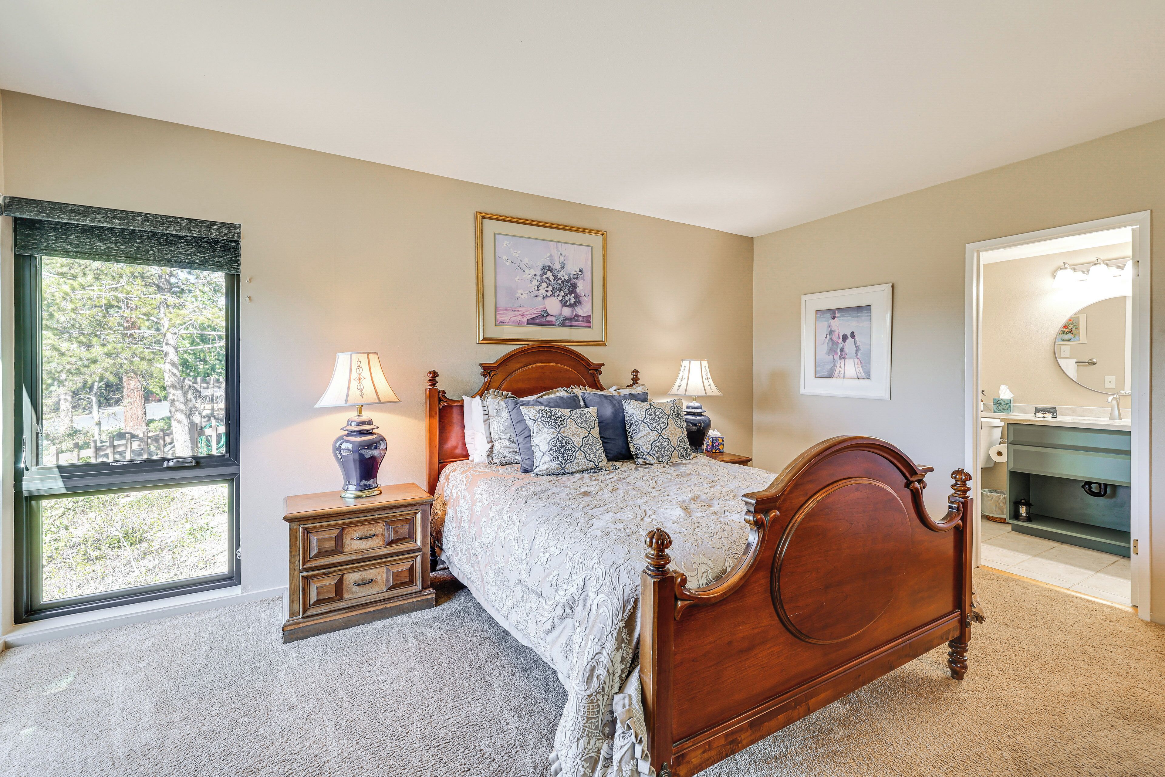 Une chambre à coucher avec un grand lit, deux tables de chevet, une fenêtre et une salle de bain visible à travers une porte ouverte.