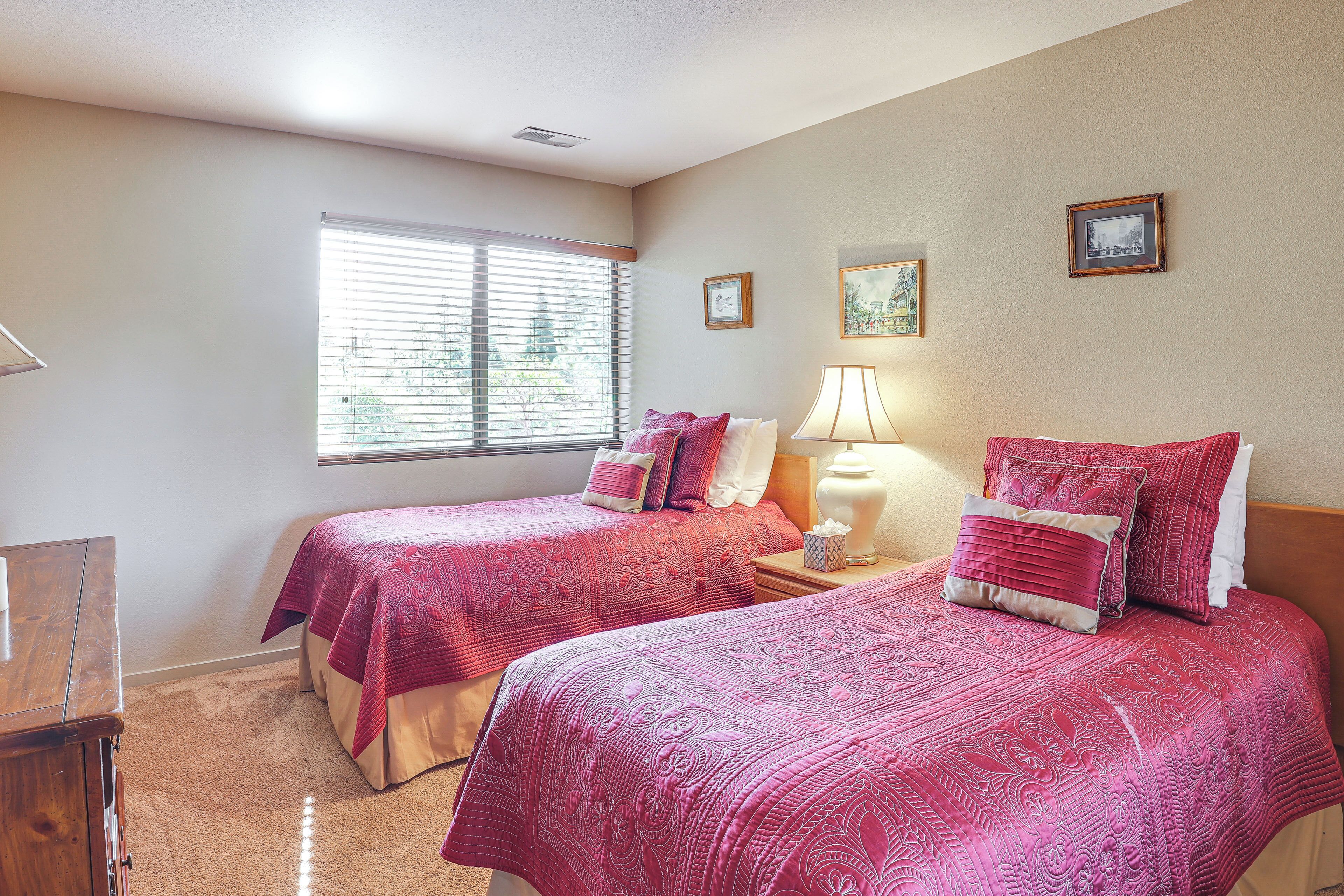 Een slaapkamer met twee bedden, een nachtkastje met een lamp en een raam met jaloezieën.