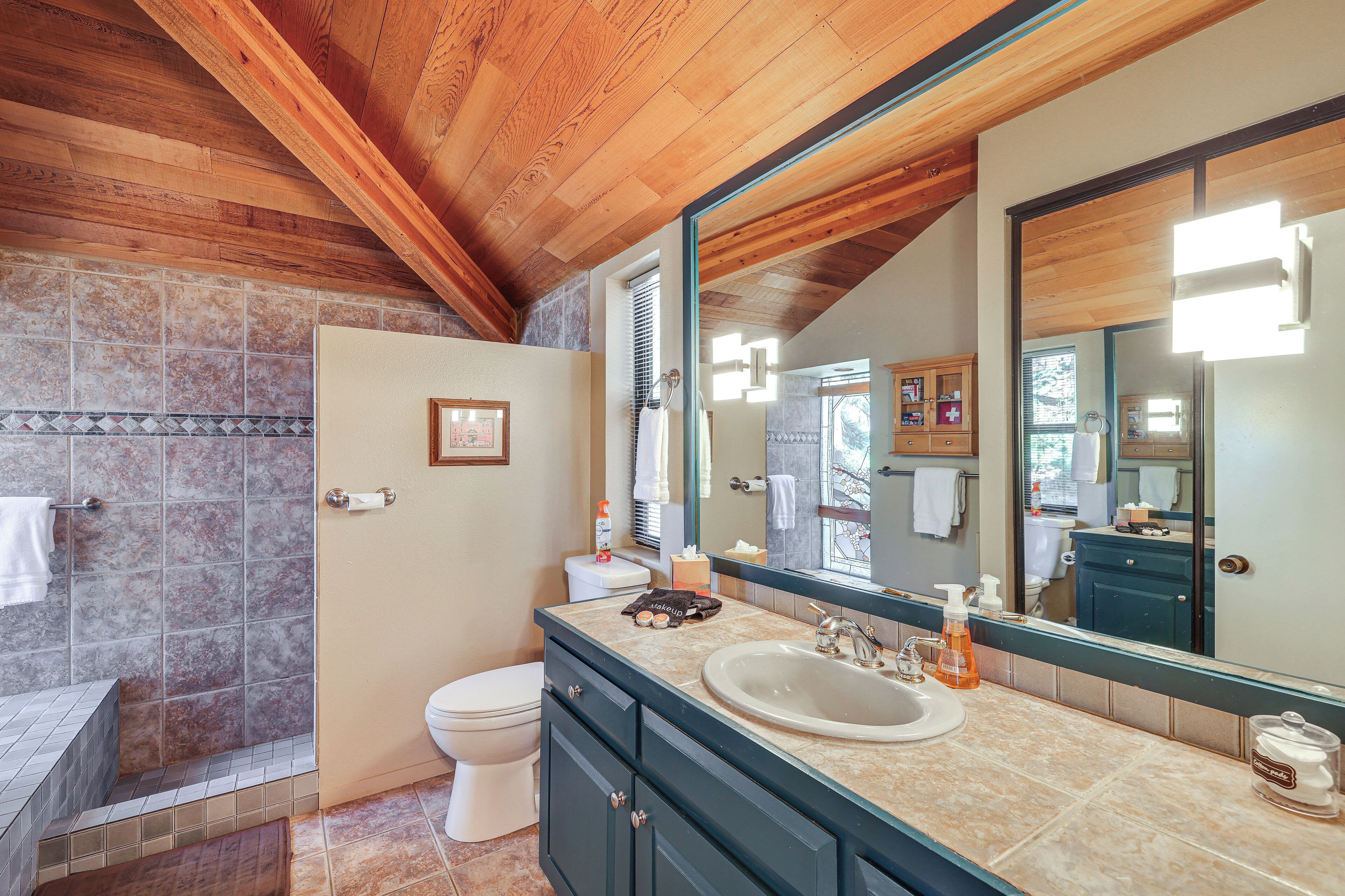 A bathroom with a wooden ceiling, a large mirror, a sink, and a toilet.